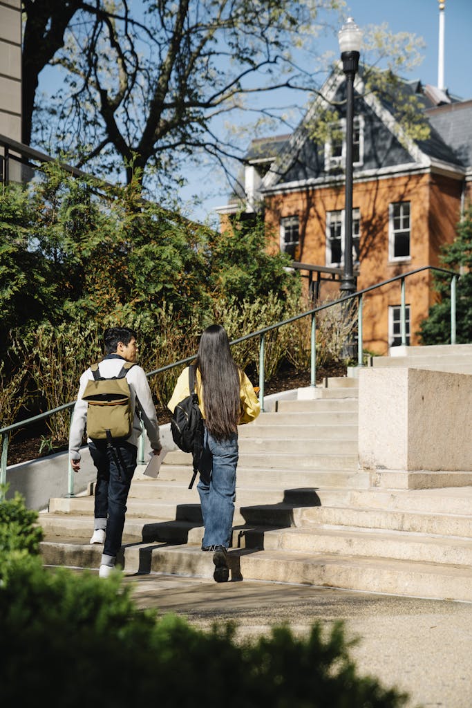 Two young adults walking up outdoor stairs surrounded by greenery and buildings.