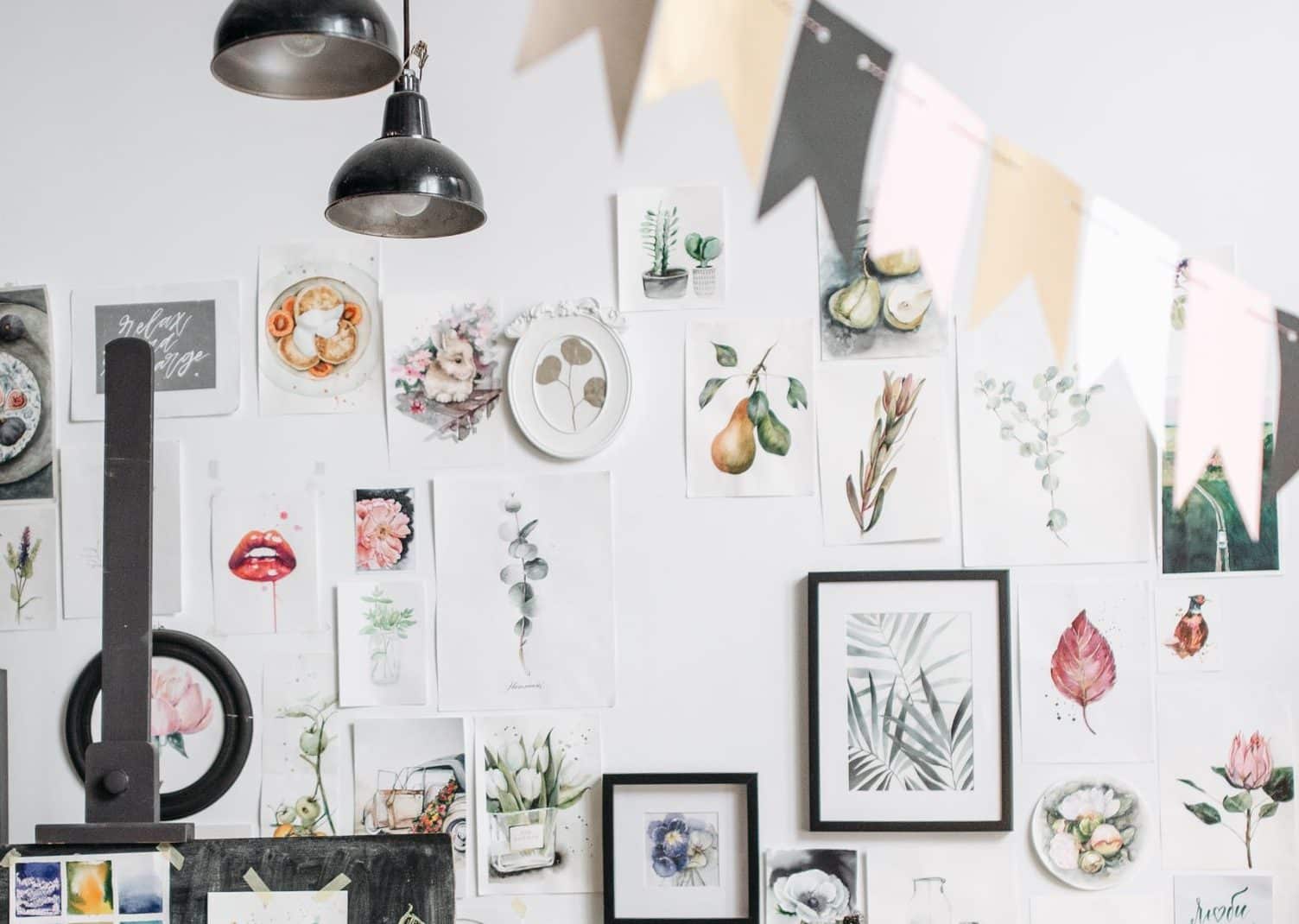 A woman art instructor in a workshop holding brushes, surrounded by art and drawings.