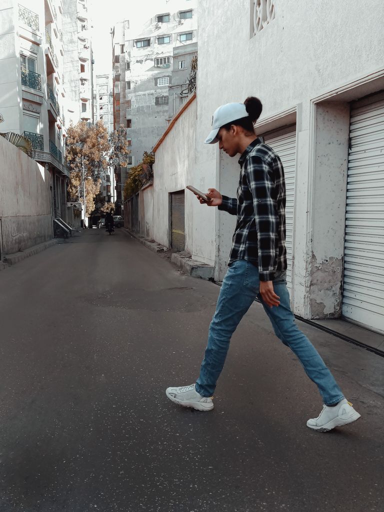 A young man walks down an urban alleyway in Istanbul, using a smartphone.